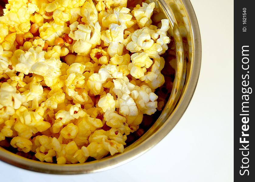 Buttered popcorn in a metal bowl on a white background