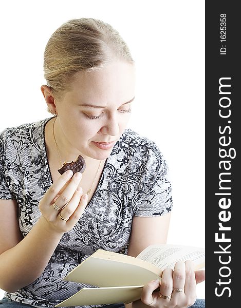 Young woman eating biscuit and reading a book on white background