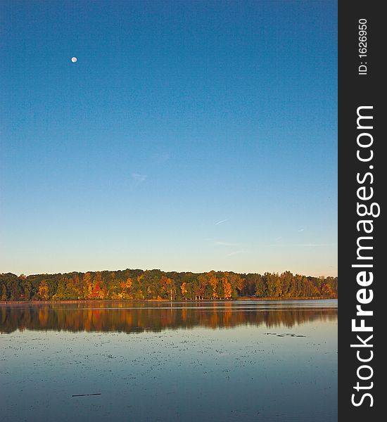 Calm pond with a crystal blue sky, autumn colors and the full moon in the background. Calm pond with a crystal blue sky, autumn colors and the full moon in the background