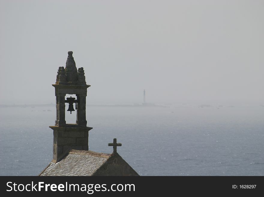 A little chapel near Pointe du Van in Bretagne (France); far away there is a lighthouse in the mist. A little chapel near Pointe du Van in Bretagne (France); far away there is a lighthouse in the mist.