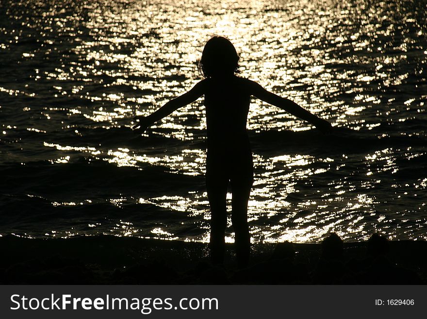 Young girl standing in surf at sunset. Young girl standing in surf at sunset