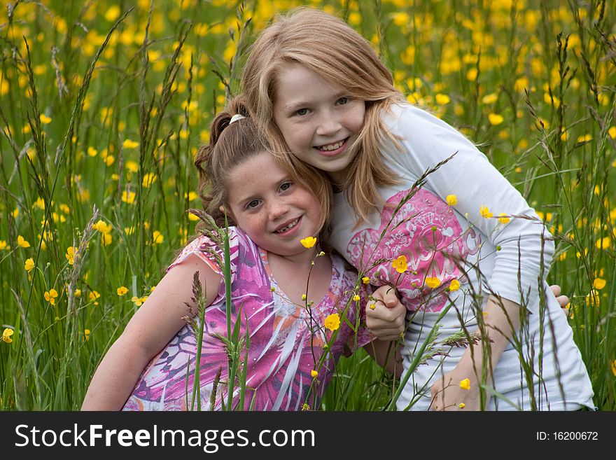 Two Beautiful young girls in a field of yellow flowers hugging eachother. Two Beautiful young girls in a field of yellow flowers hugging eachother