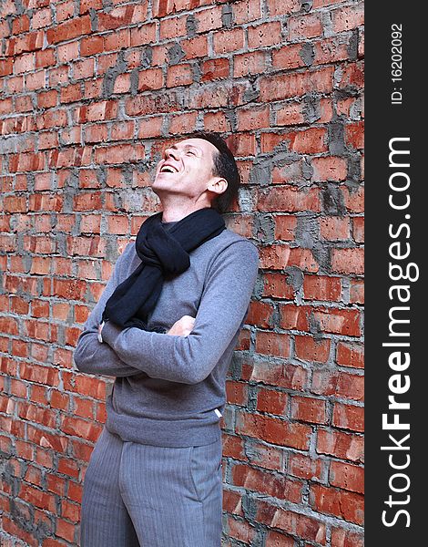 Young man in gray casual clothes laughing near brick wall. Young man in gray casual clothes laughing near brick wall.
