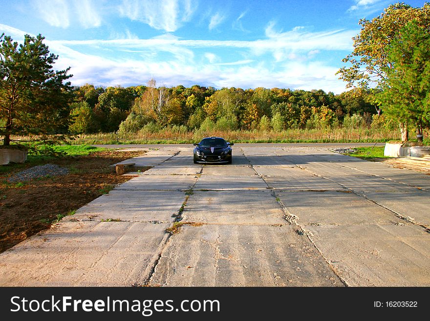 The sport black car near the forest under the sky