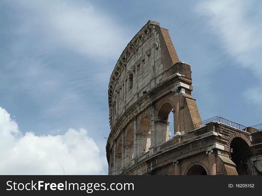 Daytime image of the Roman Coliseum with bright sun and partly cloudy skys.