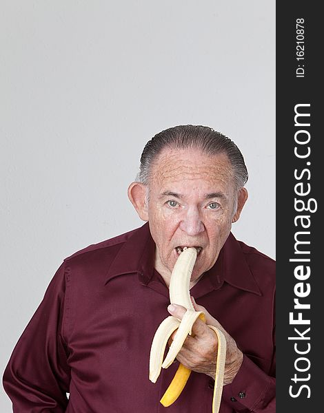 Mature man wearing a maroon shirt and eating a banana. Mature man wearing a maroon shirt and eating a banana.