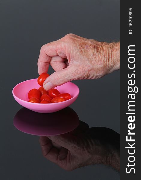 Mature male hand picking up cherry tomato from pink bowl on a black plexiglas  table.