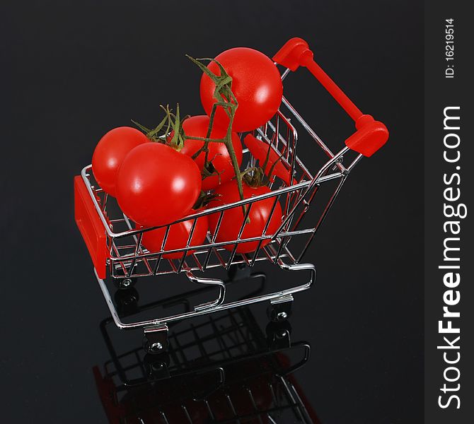 Organic tomatoes in miniature shopping cart isolated on black background with reflection. Organic tomatoes in miniature shopping cart isolated on black background with reflection