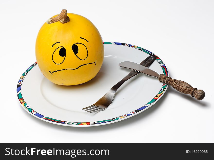 Decorative Pumpkin with a worried face drawn on it on a plate with a fork and a knife. Decorative Pumpkin with a worried face drawn on it on a plate with a fork and a knife