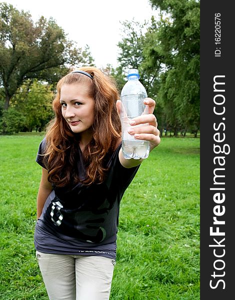 Girl on the background of fresh greens holding out a bottle of water. Girl on the background of fresh greens holding out a bottle of water