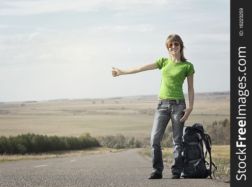 Young smiling woman with backpack catching a car on empty road