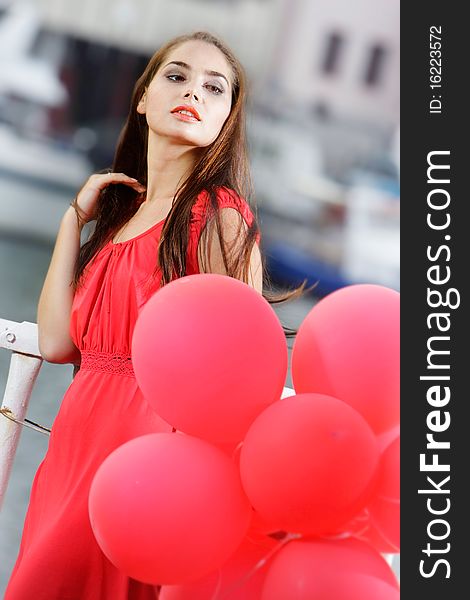 Outdoor portrait of young beautiful woman with red balloons