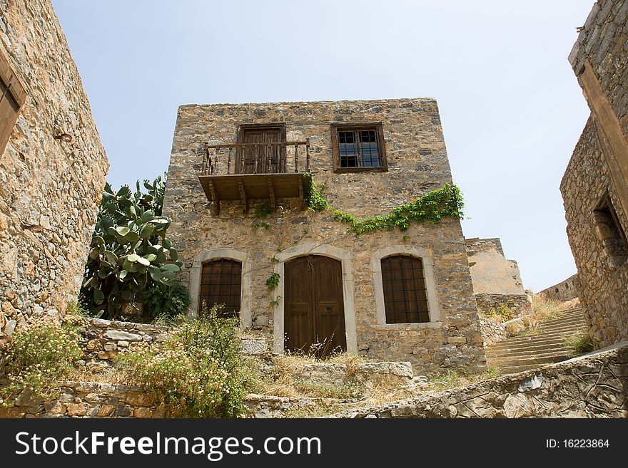 Picturesque old Mediterranean style abandoned lopsided rustic stone house with wooden sun blind, balcony in ancient town. Picturesque old Mediterranean style abandoned lopsided rustic stone house with wooden sun blind, balcony in ancient town