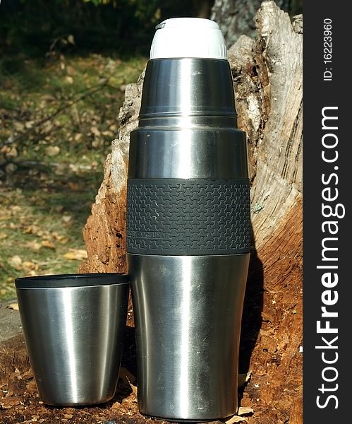 Vacuum flask and a glass on an old stump of a tree at a picnic