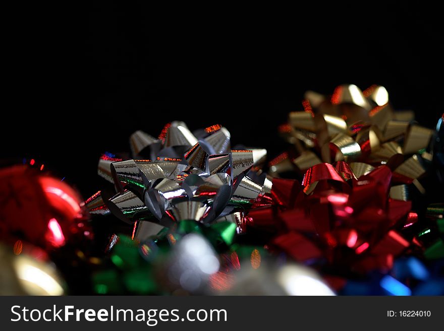 Holiday bows on a black background.  Narrow depth of field, main focus on silver bow.  Reflections on bows from colored holiday lights. Holiday bows on a black background.  Narrow depth of field, main focus on silver bow.  Reflections on bows from colored holiday lights.