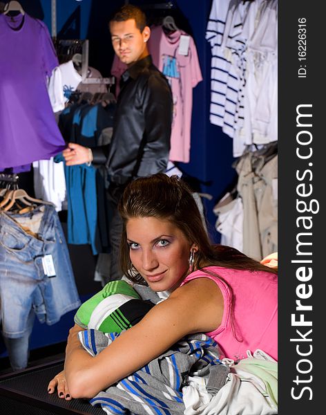 Smiling girl in dress store. She lays on shirts.