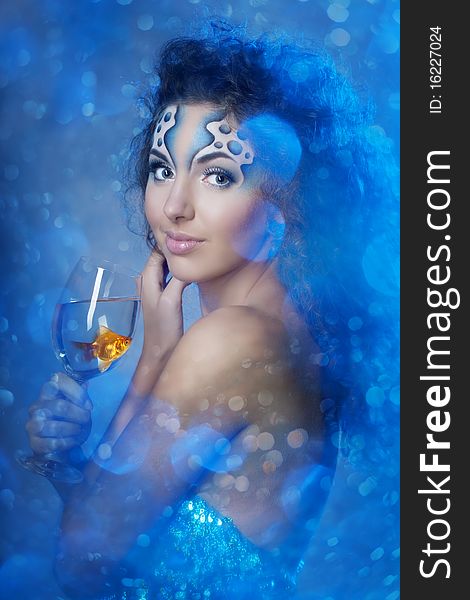 The image of a girl with makeup with a fish in a glass in her hand. The image of a girl with makeup with a fish in a glass in her hand