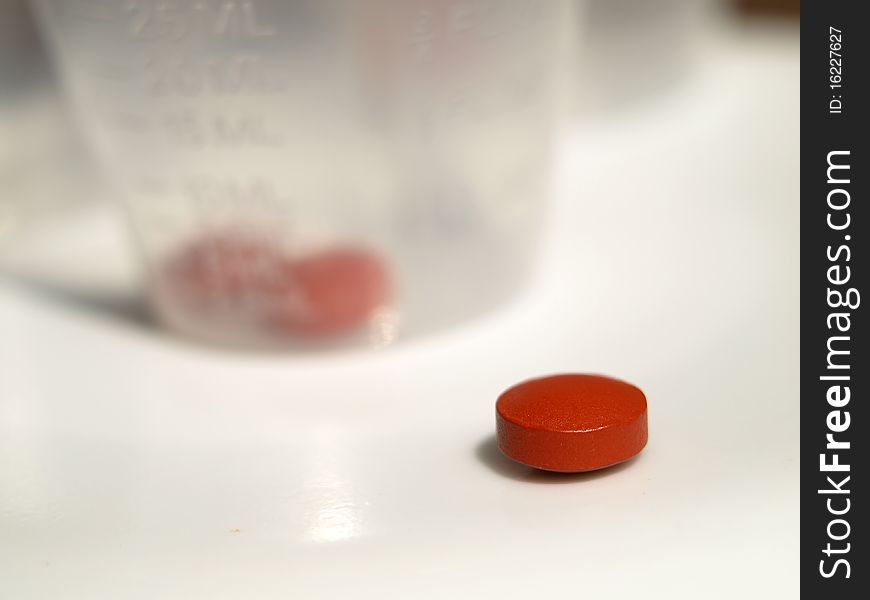 Close up shot of red tablet and medicine cup in background