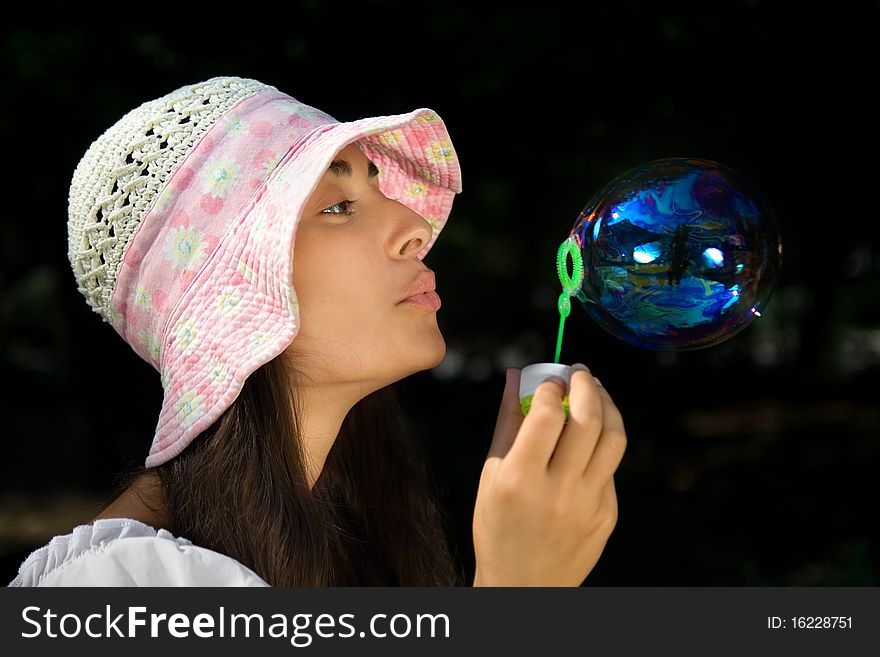 Young girl in the bonnet blowing bubbles outdoors