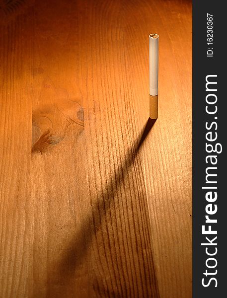 One cigarette standing on wooden background with long shadow