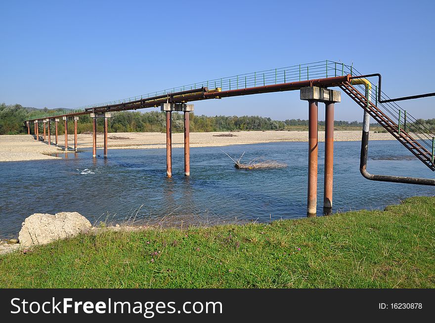 Transition of two pipelines through mountain small river in a summer landscape