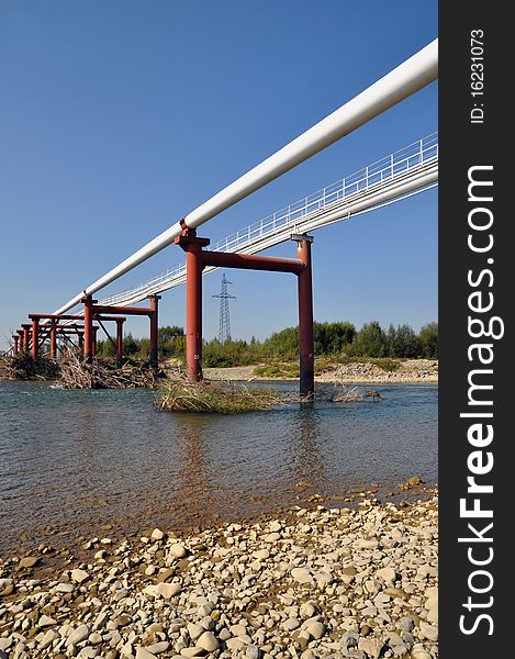 Transition of two pipelines of a high pressure through mountain small river in a summer landscape. Transition of two pipelines of a high pressure through mountain small river in a summer landscape