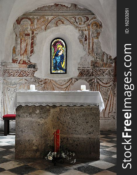 Image shows interior of a church with altar, two candles and a coloured window. Image shows interior of a church with altar, two candles and a coloured window.