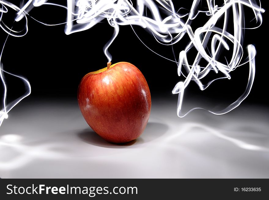 An apple sitting on a white surface with light painting streaks above and around the apple. An apple sitting on a white surface with light painting streaks above and around the apple.