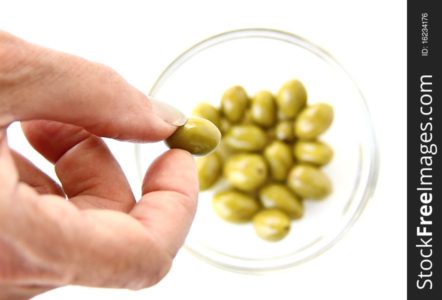 A hand carrying a green olive over a bowl isolated on white background