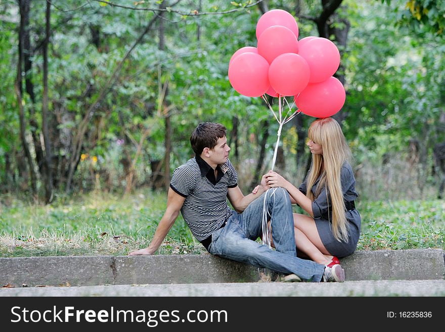 Young loving couple with red balloons on natural background