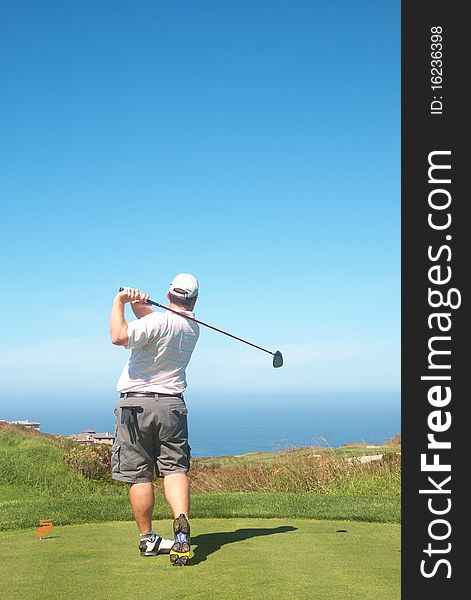 Young male golfer hitting the ball from the tee box next to the ocean on a beautiful summer day. Young male golfer hitting the ball from the tee box next to the ocean on a beautiful summer day