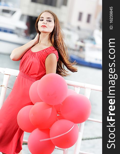 Young beautiful woman with red balloons on urban background