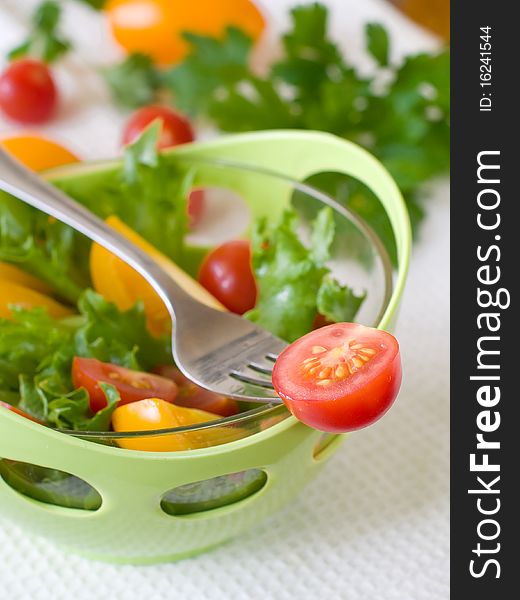 A fresh ripe tomato on a fork with bowl of salad on backround. A fresh ripe tomato on a fork with bowl of salad on backround