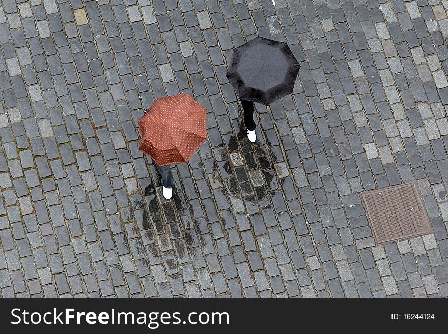 Two persons with umbrellas walking on wet paving stone. Two persons with umbrellas walking on wet paving stone