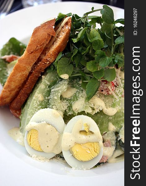 Caesar Salad on a white plate with egg and crusty bread