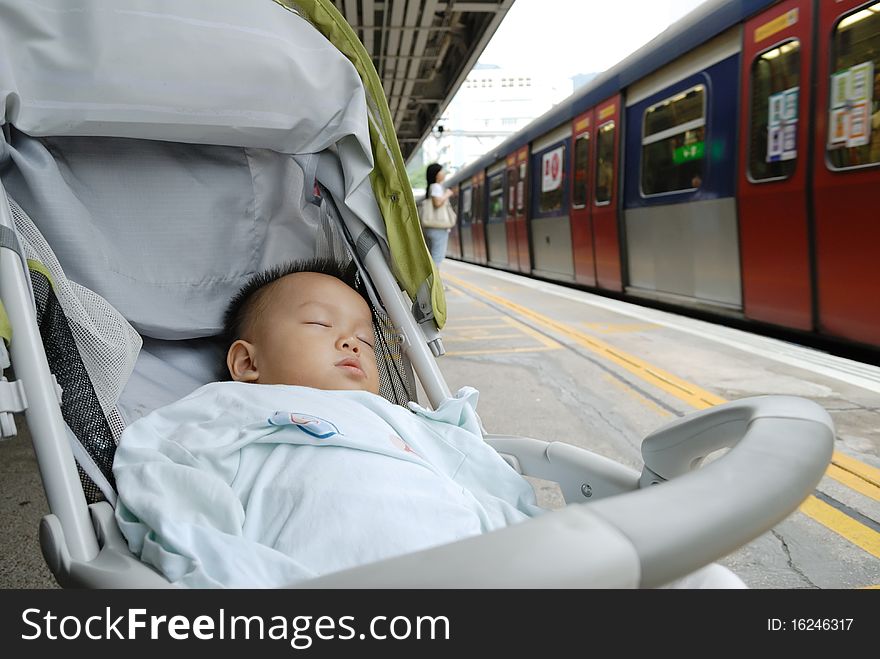 In the platform, a chinese boy is sleeping in the baby carrier when waiting the train. In the platform, a chinese boy is sleeping in the baby carrier when waiting the train.