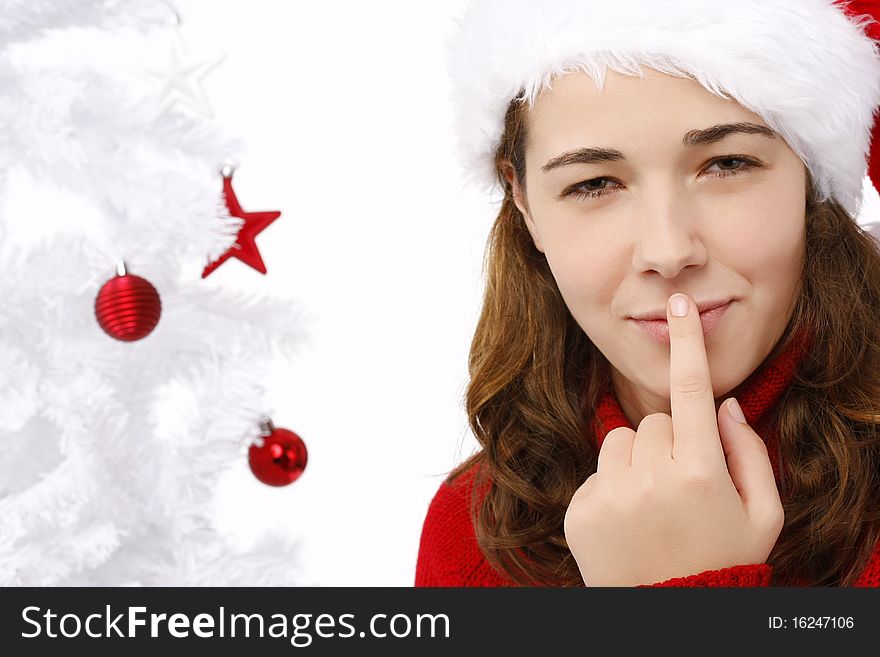 Beautiful young woman wearing santa hat next to christmas tree on white background