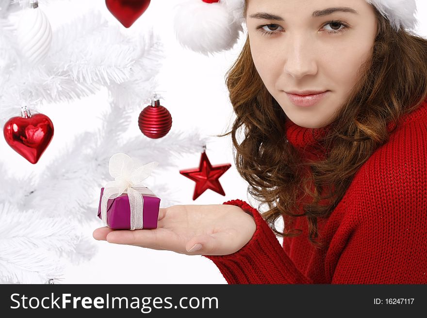 Beautiful young woman wearing santa hat next to christmas tree holding a christmas gift