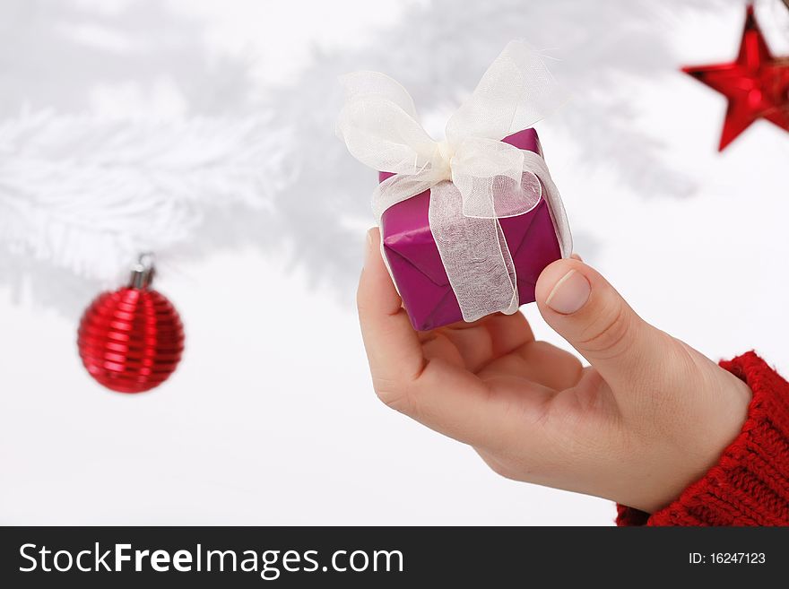 Hand holding a christmas gift with a white christmas tree in the background