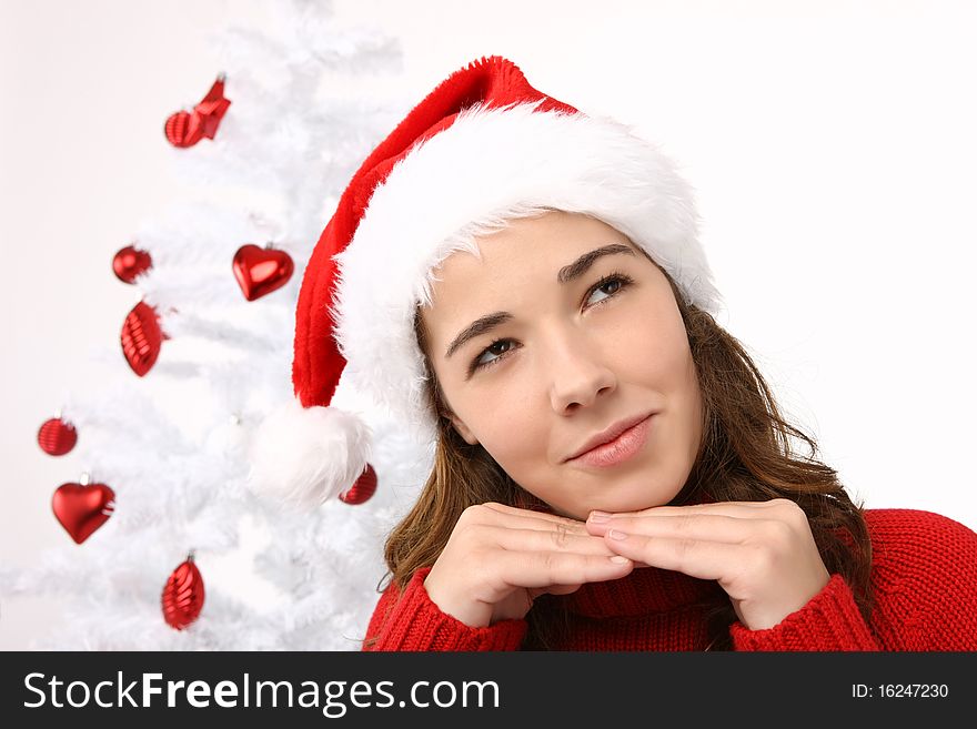 Beautiful young woman wearing santa hat next to christmas tree on white background