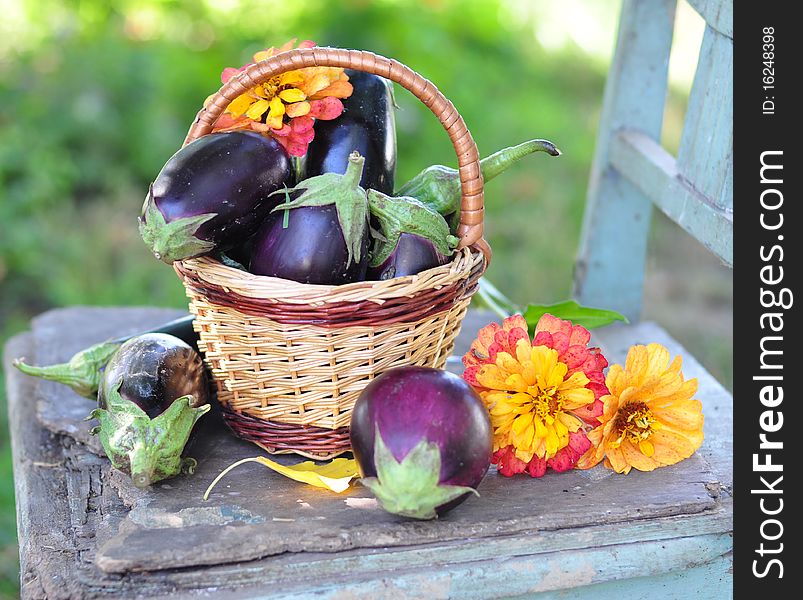 Egg-plants are in a small basket, alongside three flowers. Egg-plants are in a small basket, alongside three flowers