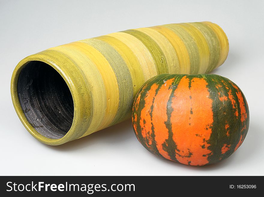 The striped pumpkin lies near to a striped vase