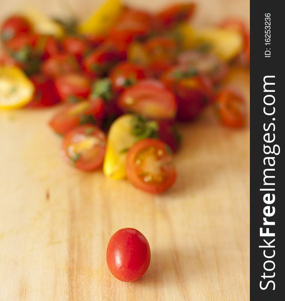 One tomato resting in front of a group of chopped yellow and red tomatoes, cilantro sprinkled with lime on a wooden cutting board. One tomato resting in front of a group of chopped yellow and red tomatoes, cilantro sprinkled with lime on a wooden cutting board