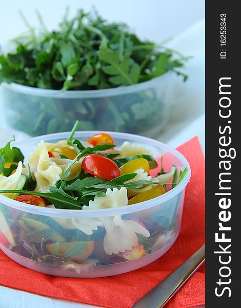 Salad with tomatoes and arugula and pasta in a glass bowl