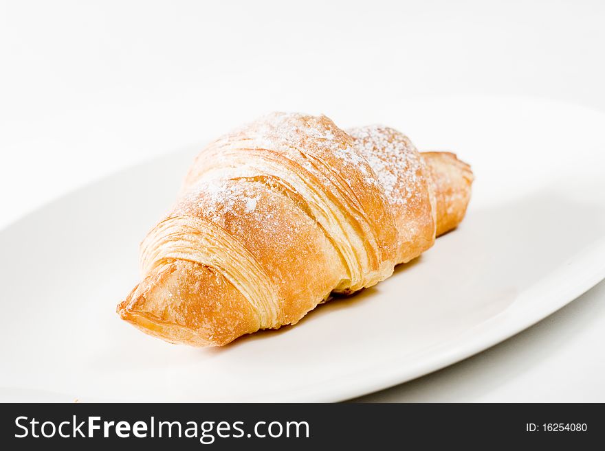 Fresh croissant on white plate with powdered sugar