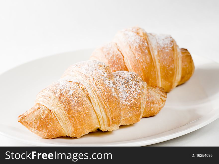 Fresh croissants on white plate with powdered sugar .