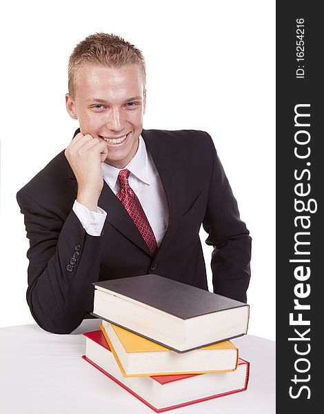 A young business man sitting at a table with a stack of books reading and showing a happy expression. A young business man sitting at a table with a stack of books reading and showing a happy expression.