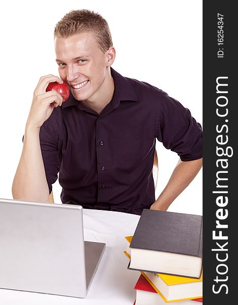 A young man sitting by his computer getting ready to eat a fruit with a happy expression on his face. A young man sitting by his computer getting ready to eat a fruit with a happy expression on his face.
