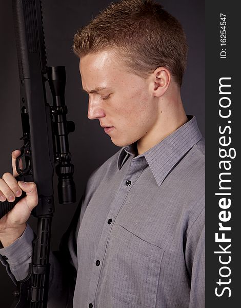 A young man holding a gun looking down at the trigger. A young man holding a gun looking down at the trigger.