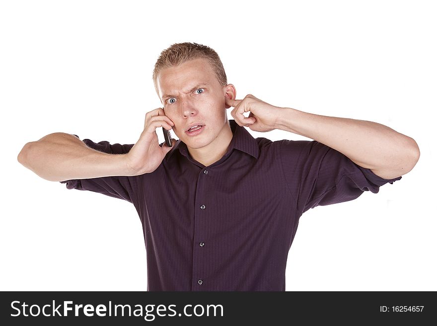 A young man plugging his ears trying to  listen to the person on his phone. A young man plugging his ears trying to  listen to the person on his phone.